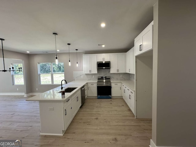 kitchen featuring light wood-type flooring, stainless steel appliances, sink, kitchen peninsula, and decorative light fixtures