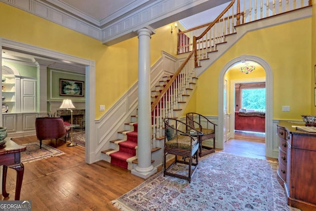 staircase with ornate columns, crown molding, a fireplace, and hardwood / wood-style floors