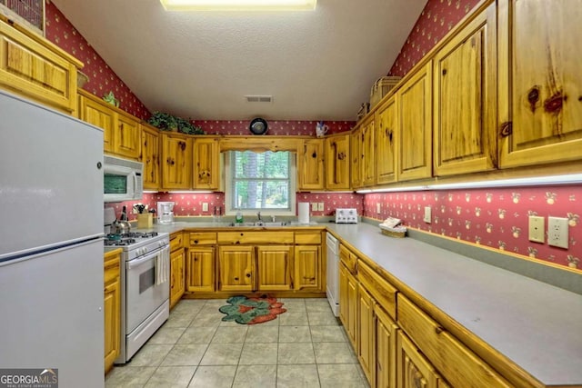 kitchen featuring sink, white appliances, a textured ceiling, and light tile patterned floors