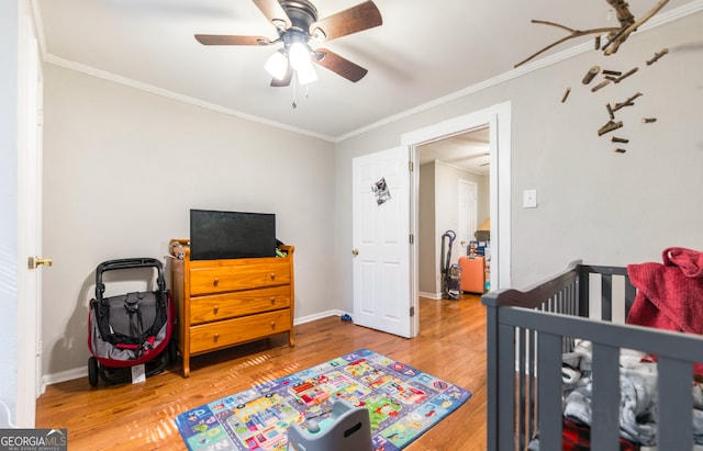 bedroom featuring ceiling fan, hardwood / wood-style floors, crown molding, and a crib