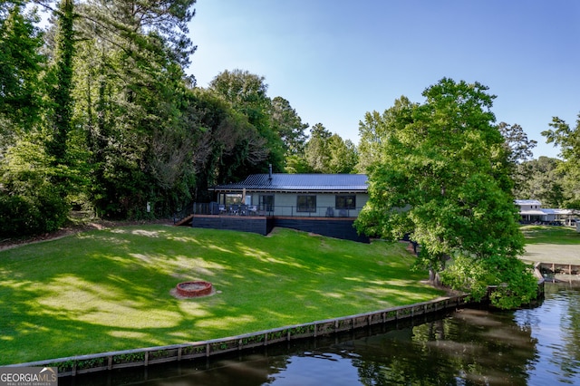 rear view of house with a water view, a fire pit, and a lawn