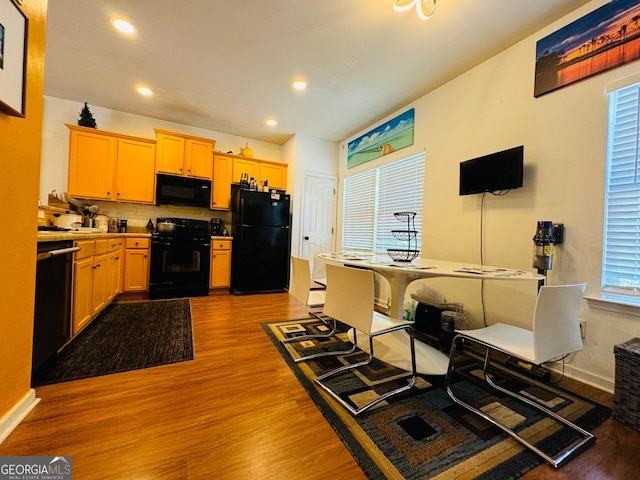 kitchen featuring backsplash, black appliances, hardwood / wood-style floors, and light brown cabinets