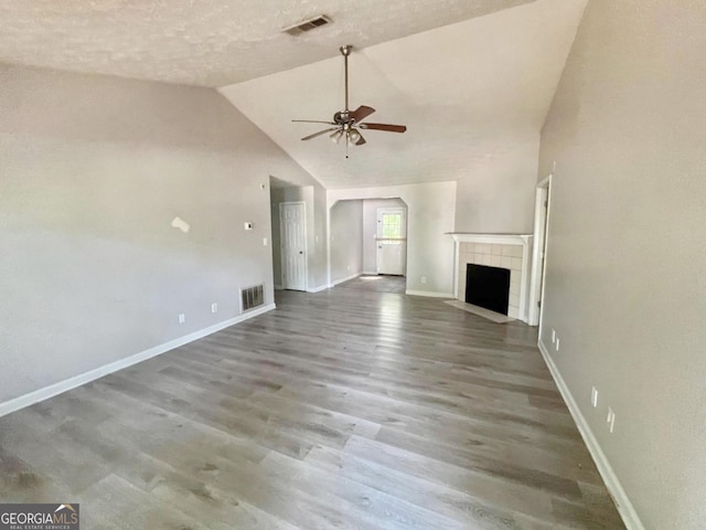 unfurnished living room featuring a tile fireplace, vaulted ceiling, hardwood / wood-style floors, ceiling fan, and a textured ceiling