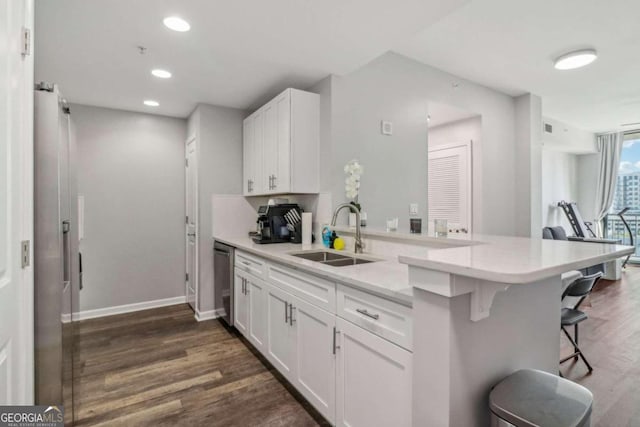 kitchen with a kitchen bar, kitchen peninsula, stainless steel dishwasher, sink, and white cabinets