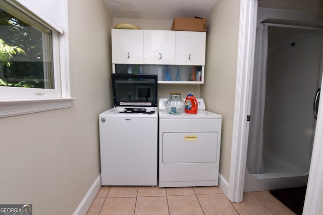 washroom with cabinets, a textured ceiling, washing machine and dryer, and light tile patterned flooring