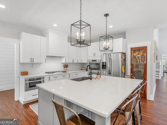 kitchen with appliances with stainless steel finishes, dark hardwood / wood-style floors, a kitchen breakfast bar, and an island with sink