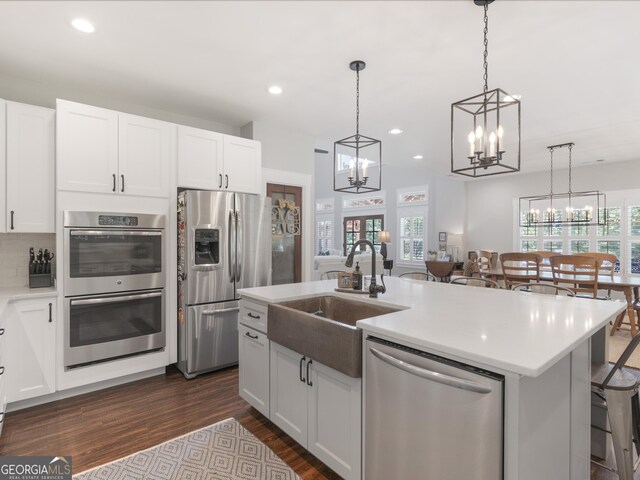 kitchen with white cabinetry, dark wood-type flooring, an island with sink, stainless steel appliances, and pendant lighting