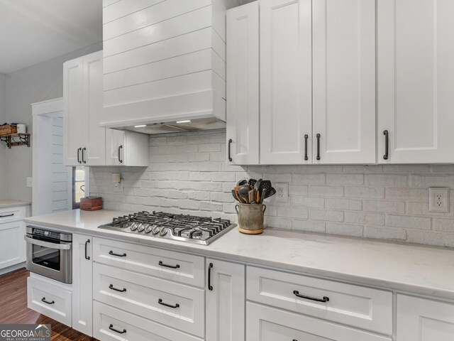 kitchen with premium range hood, stainless steel appliances, white cabinets, dark hardwood / wood-style floors, and backsplash