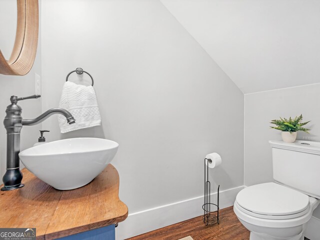 bathroom featuring sink, hardwood / wood-style flooring, toilet, and vaulted ceiling