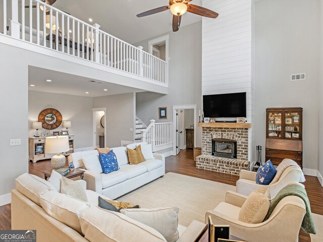 living room with dark wood-type flooring, a towering ceiling, and a brick fireplace