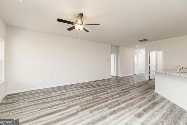 unfurnished living room with ceiling fan, light wood-type flooring, and sink