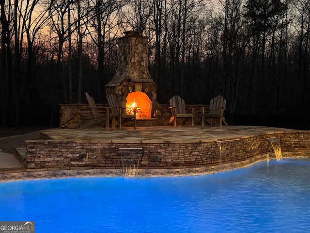 view of swimming pool with a patio area, pool water feature, and an outdoor stone fireplace