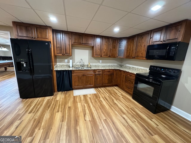 kitchen with light stone counters, a paneled ceiling, black appliances, light wood-type flooring, and sink