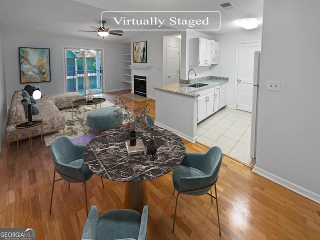 kitchen featuring ceiling fan, sink, light stone counters, refrigerator, and white cabinets