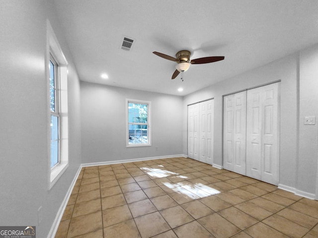 unfurnished bedroom with light tile patterned floors, two closets, and ceiling fan