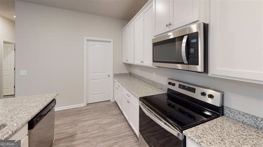 kitchen with light stone countertops, appliances with stainless steel finishes, white cabinetry, and light hardwood / wood-style floors