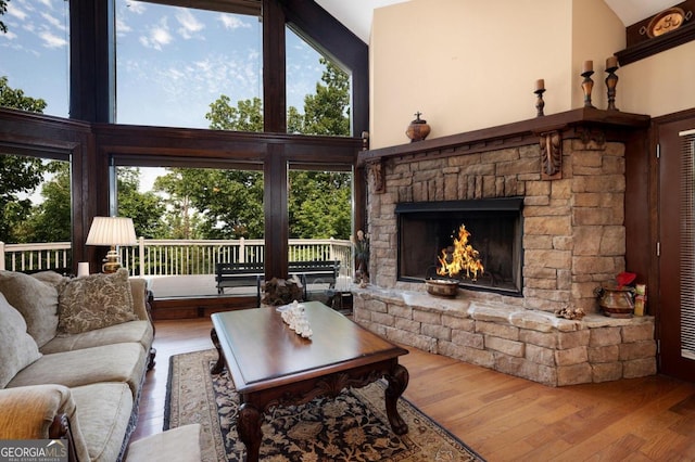 living room with high vaulted ceiling, plenty of natural light, hardwood / wood-style floors, and a fireplace