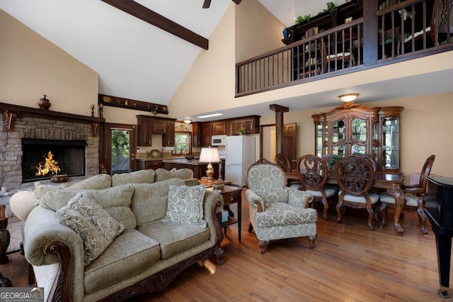 living room with high vaulted ceiling, light wood-type flooring, a stone fireplace, and beam ceiling