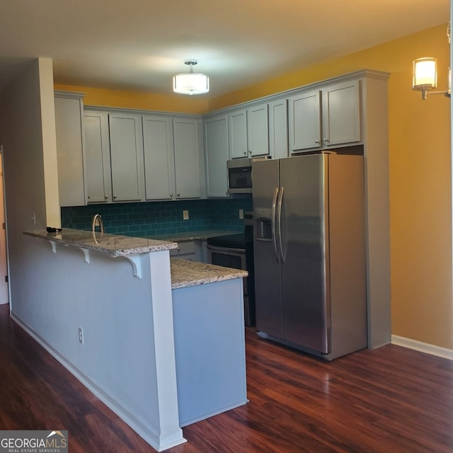 kitchen featuring kitchen peninsula, backsplash, light stone countertops, dark wood-type flooring, and appliances with stainless steel finishes