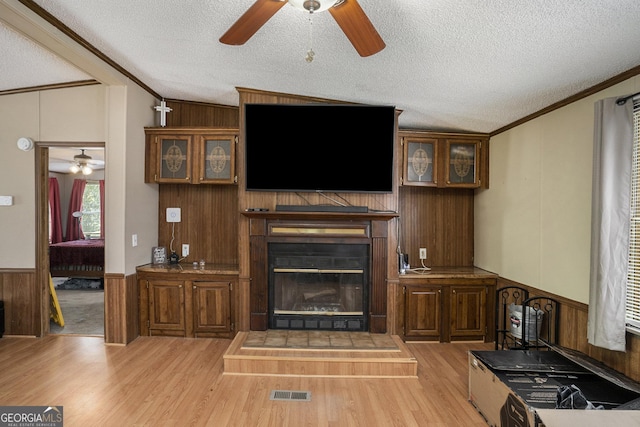 living room with ornamental molding, wooden walls, a textured ceiling, and light hardwood / wood-style flooring