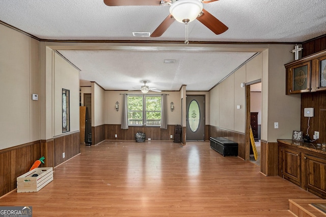 living room with ornamental molding, light hardwood / wood-style floors, a textured ceiling, and wood walls