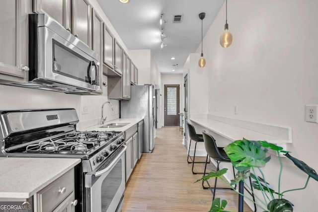 kitchen with sink, hanging light fixtures, light wood-type flooring, appliances with stainless steel finishes, and rail lighting