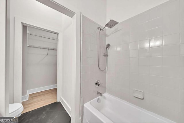 bathroom featuring toilet, tiled shower / bath combo, and tile patterned flooring