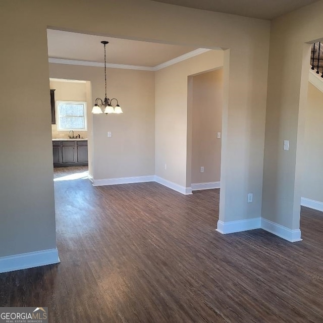 spare room with a notable chandelier, dark wood-style flooring, a sink, baseboards, and crown molding