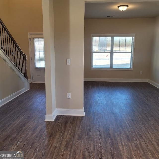 spare room with dark wood-style flooring, visible vents, baseboards, and stairs