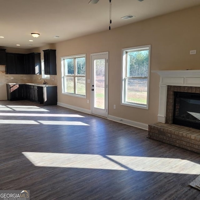 unfurnished living room featuring a brick fireplace, sink, dark hardwood / wood-style floors, and ceiling fan