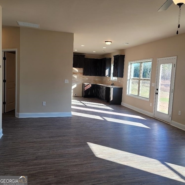 interior space featuring dark wood-style flooring, tasteful backsplash, open floor plan, dark cabinetry, and baseboards