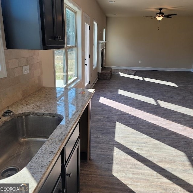 kitchen with light stone countertops, dark wood-type flooring, decorative backsplash, sink, and ceiling fan