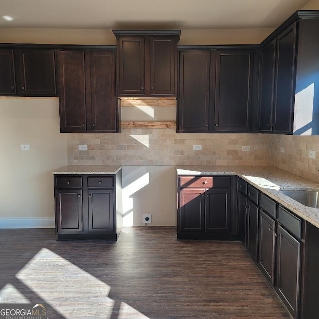 kitchen featuring dark hardwood / wood-style flooring, decorative backsplash, dark brown cabinetry, and light stone countertops