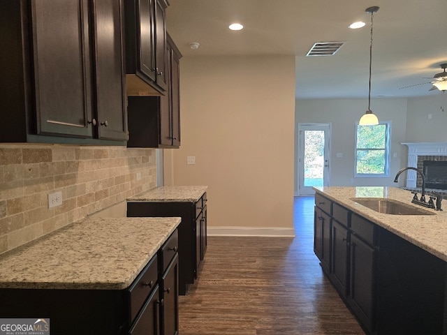 kitchen featuring light stone counters, dark hardwood / wood-style floors, sink, hanging light fixtures, and a kitchen island