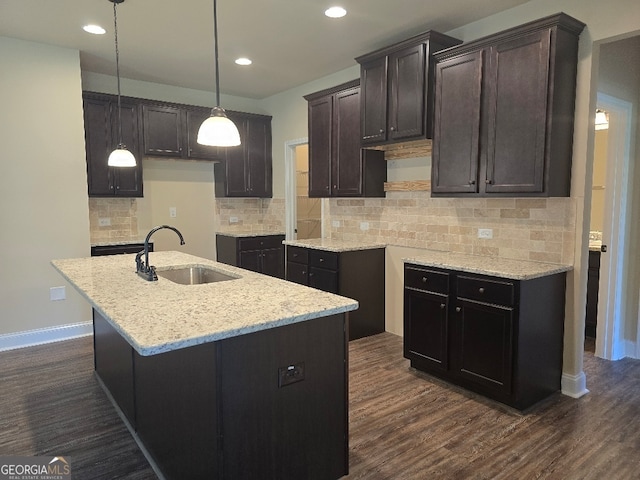 kitchen with dark wood-type flooring, tasteful backsplash, pendant lighting, a center island with sink, and sink