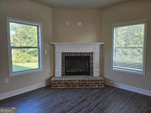 unfurnished living room featuring a brick fireplace, dark hardwood / wood-style floors, and plenty of natural light