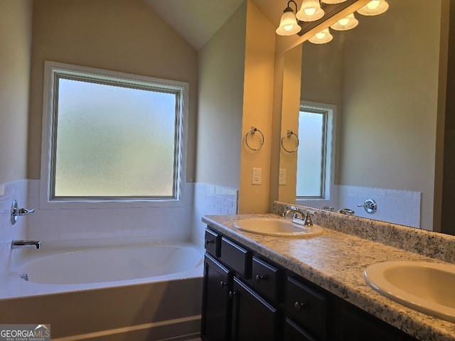 bathroom with tile walls, vaulted ceiling, a washtub, and vanity