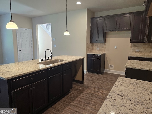 kitchen with backsplash, hanging light fixtures, a kitchen island with sink, and sink