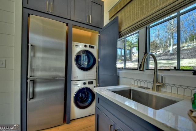 washroom with light hardwood / wood-style flooring, stacked washer and clothes dryer, and sink