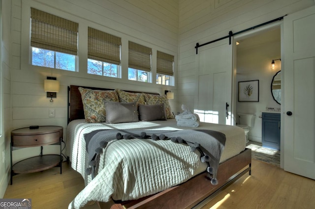 bedroom with a barn door, light hardwood / wood-style floors, multiple windows, and connected bathroom