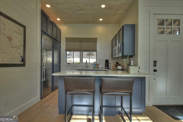 kitchen featuring kitchen peninsula, appliances with stainless steel finishes, wooden ceiling, and a breakfast bar area