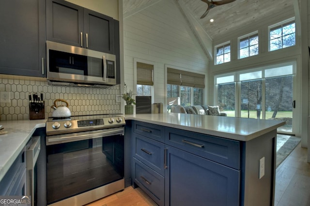 kitchen featuring ceiling fan, stainless steel appliances, tasteful backsplash, light hardwood / wood-style flooring, and high vaulted ceiling