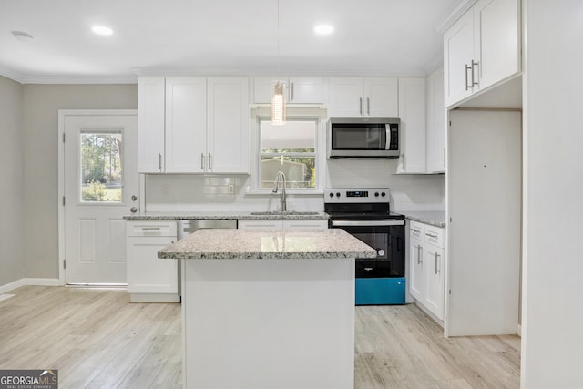 kitchen with sink, light stone countertops, appliances with stainless steel finishes, a kitchen island, and white cabinetry