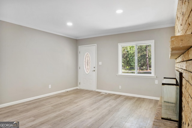 foyer entrance with a large fireplace, ornamental molding, and light hardwood / wood-style flooring