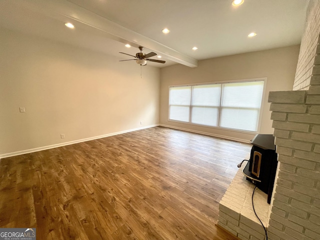 unfurnished living room with beamed ceiling, hardwood / wood-style flooring, a wood stove, and ceiling fan