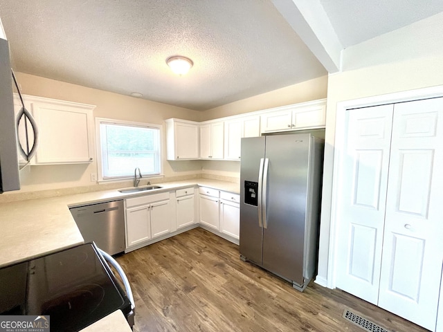 kitchen with sink, a textured ceiling, appliances with stainless steel finishes, white cabinetry, and wood-type flooring