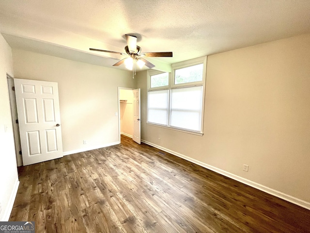 unfurnished bedroom with a walk in closet, a textured ceiling, dark hardwood / wood-style floors, and ceiling fan