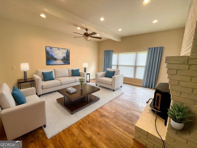 living room with beamed ceiling, ceiling fan, light wood-type flooring, and a wood stove