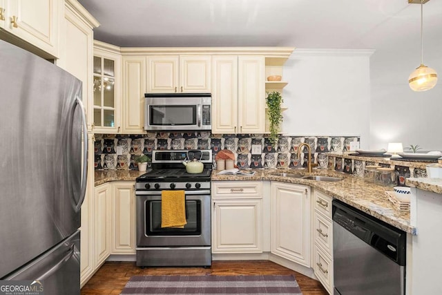 kitchen with stainless steel appliances, cream cabinetry, sink, light stone counters, and dark wood-type flooring