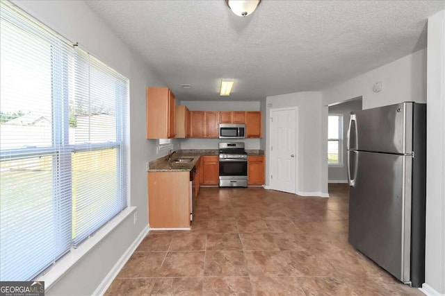 kitchen with a textured ceiling, stainless steel appliances, dark stone countertops, and sink